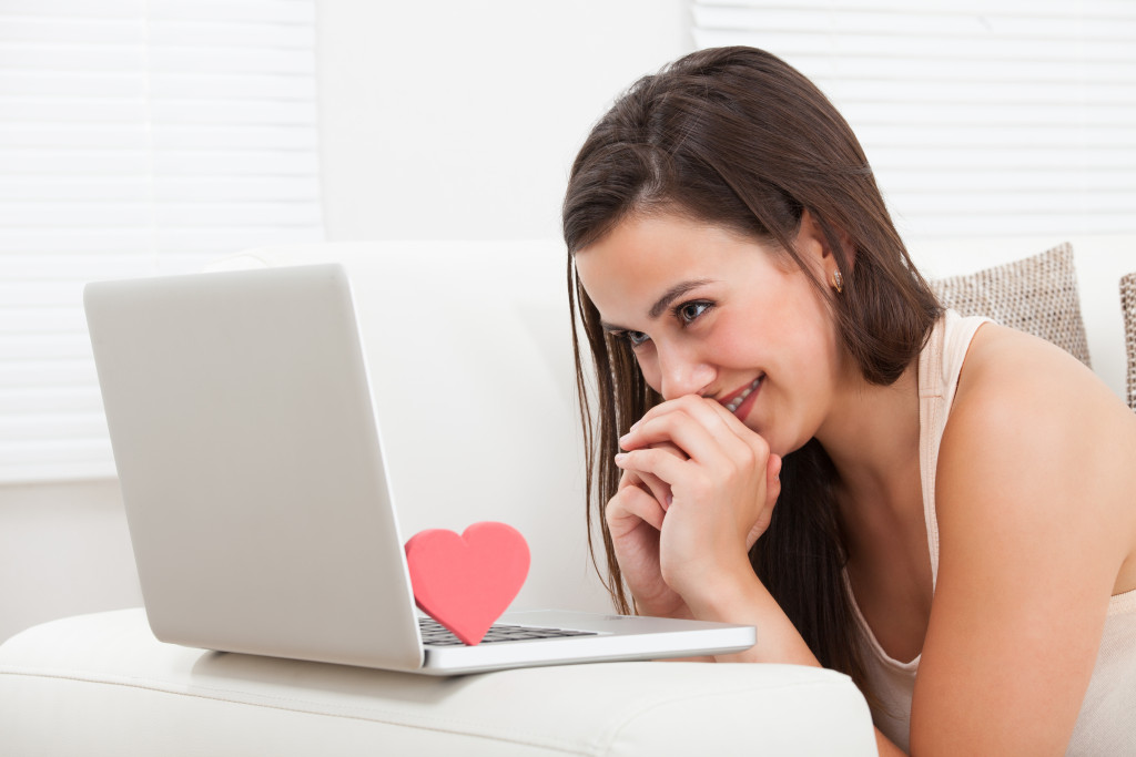 a beautiful young woman happily looking at her laptop that has a heart on top