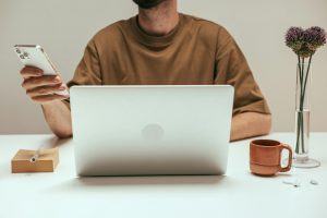 man using a phone while sitting in front of a laptop