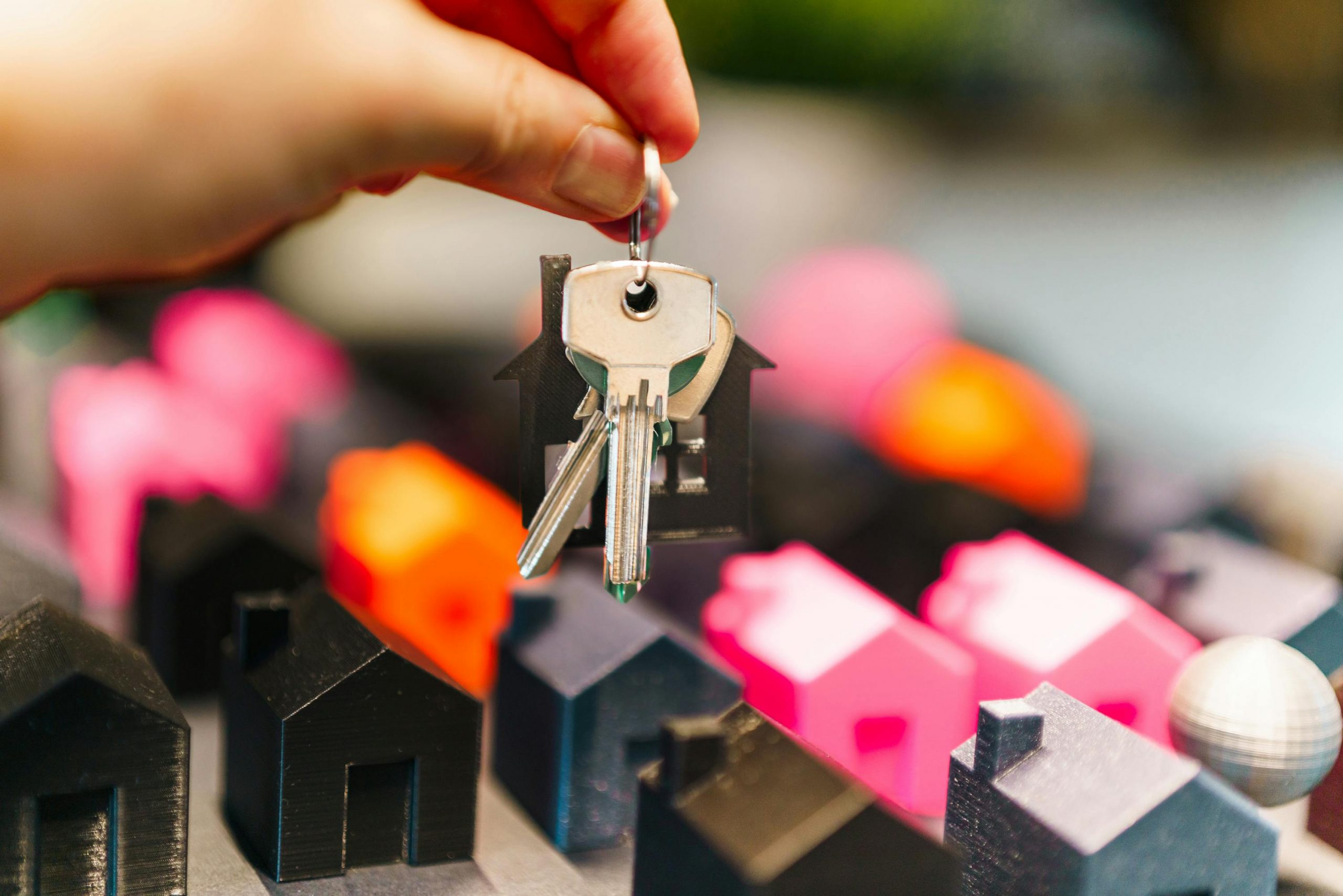 person holding keys over miniature houses